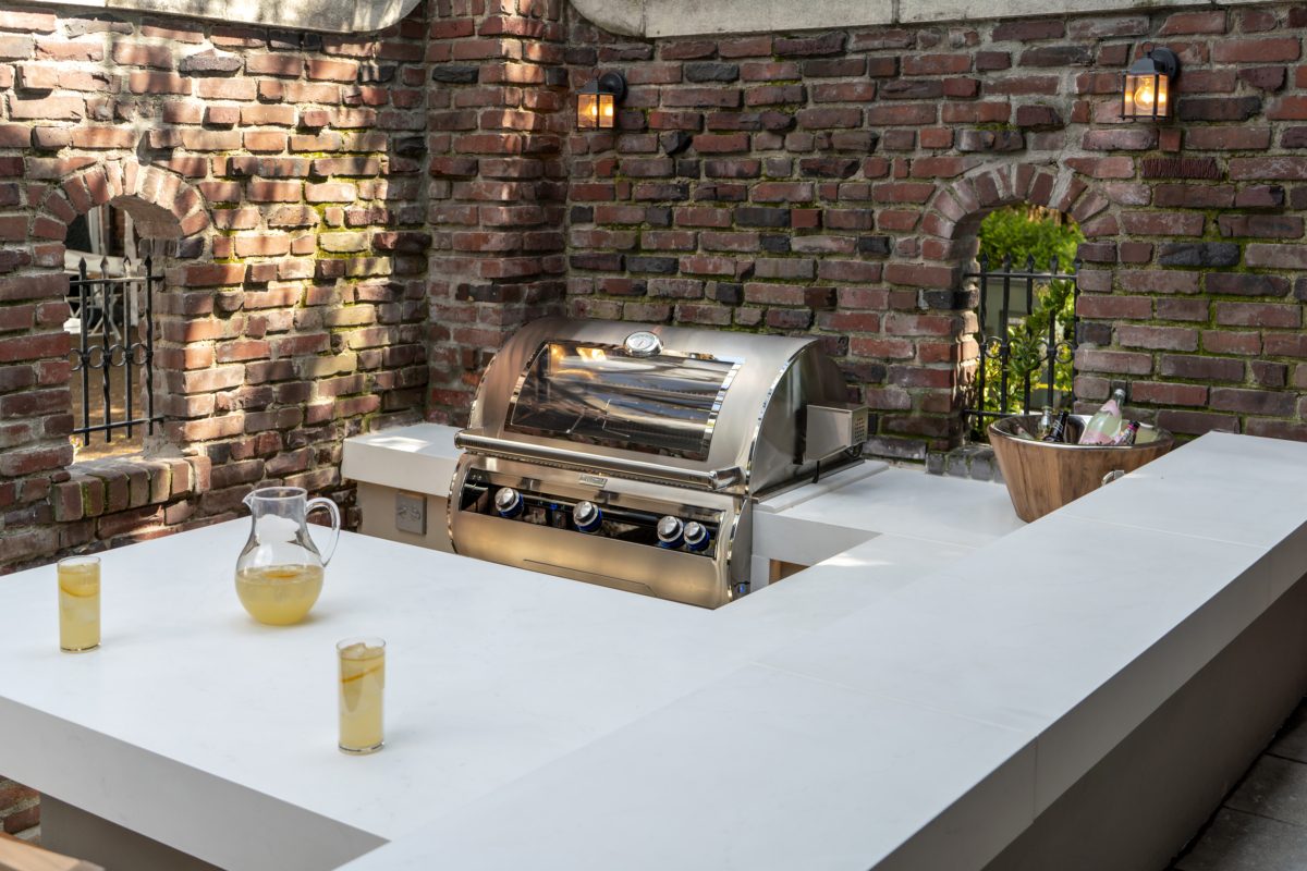 Fire Magic Echelon grill built into a stone outdoor kitchen against brick