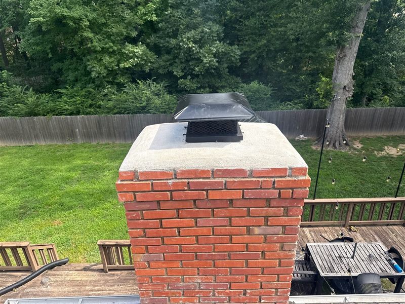 Red brick chimney with fresh concrete crown and black stainless cap by Madewell Masonry in Memphis
