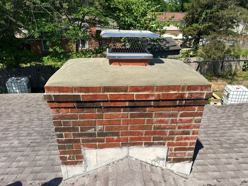 Finished poured concrete chimney crown sloped away from the flue with an overhanging drip edge and a new stainless steel cap with mesh