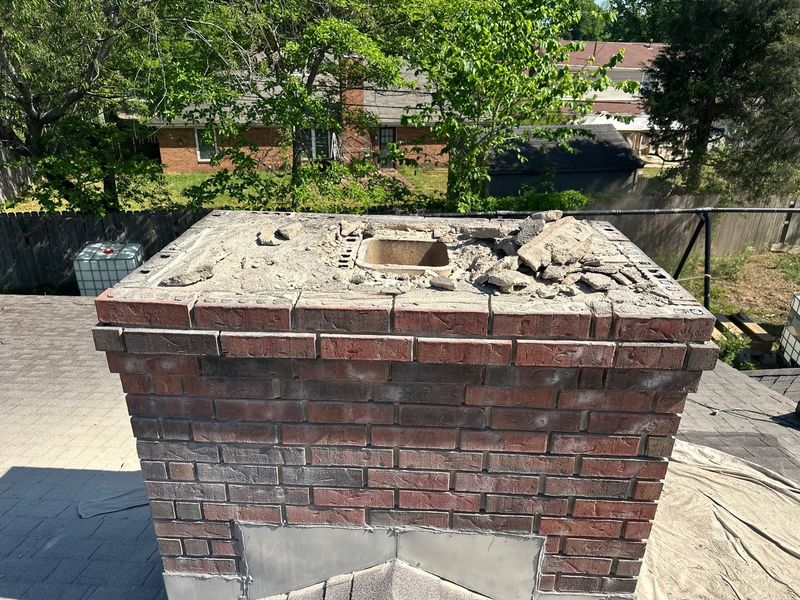 Old cracked chimney crown broken out with concrete debris on top and the clay flue tile opening exposed before a new crown is poured
