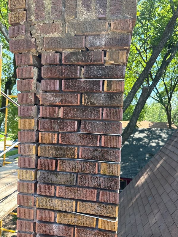Scaffolding erected beside a brick chimney showing a vertical crack running down the corner with displaced brick and open mortar joints