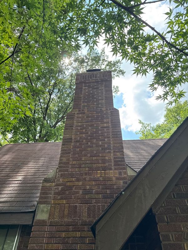 Completed brick chimney rebuild viewed from the ground, with decorative corbelled banding, new crown and black cap against the sky