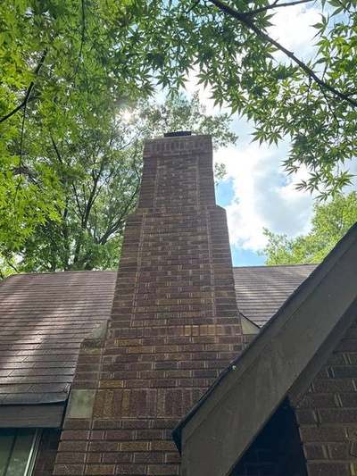 Completed brick chimney rebuild viewed from the ground, with decorative corbelled banding, new crown and black cap against the sky