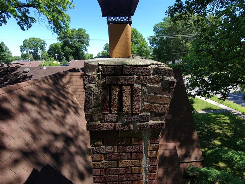 Pre-repair brick chimney with sound brick units, washed-out mortar joints, and failed gray surface patchwork that did not stop the stack from coming apart