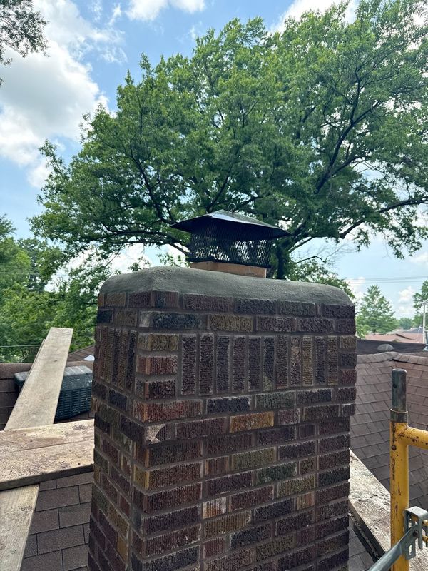 Newly poured sloped concrete chimney crown with overhanging drip edge and a black stainless steel cap with mesh spark arrestor after Madewell rebuild