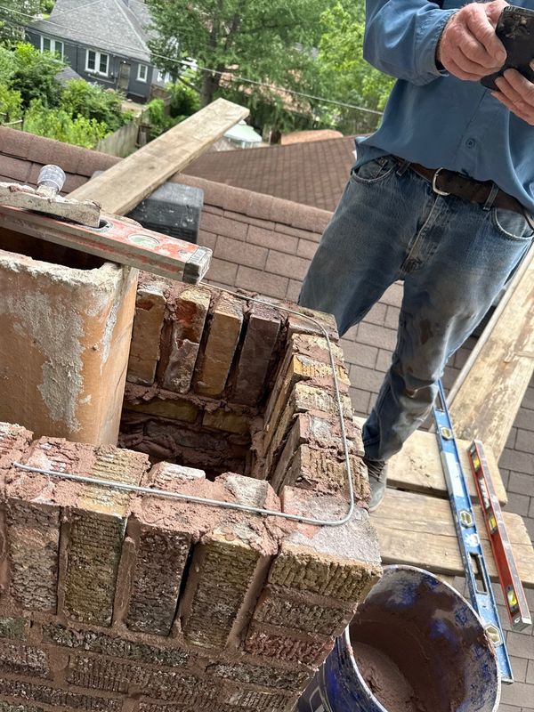 Rebuilt chimney top course with a ring of steel reinforcement wire laid around its perimeter beside the clay flue tile, levels resting on the brickwork