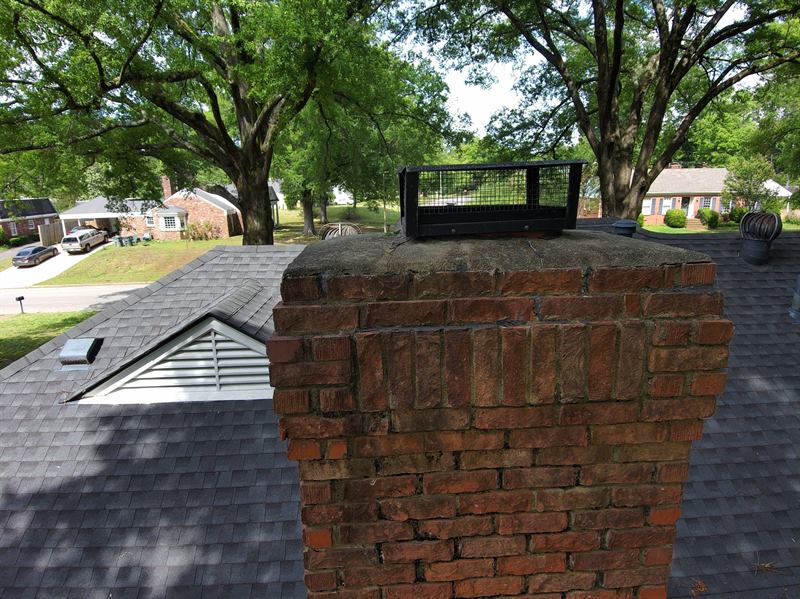 Brick chimney with worn crown and black mesh cap before Madewell rebuild in Memphis