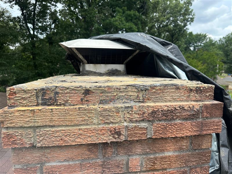 Failed chimney crown with heavily spalled brick and temporary black tarp before Madewell crown rebuild in Memphis