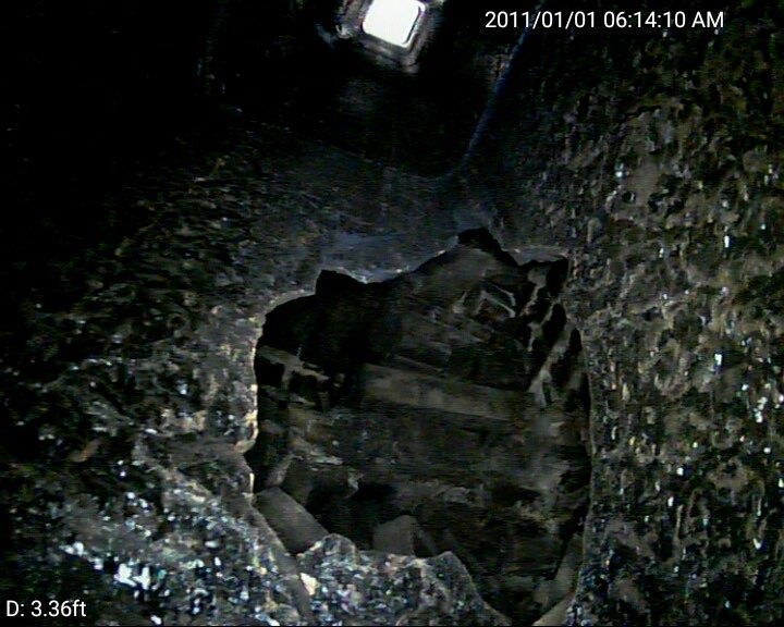Chimney camera still a few feet up the same flue showing a large hole through the clay tile liner with brick masonry visible behind the breach