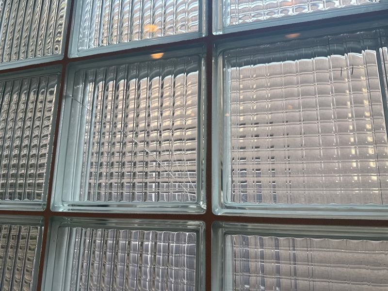 Close view of a cracked glass block set in brown mortar joints, with a diagonal crack across one unit in a Memphis glass-block wall