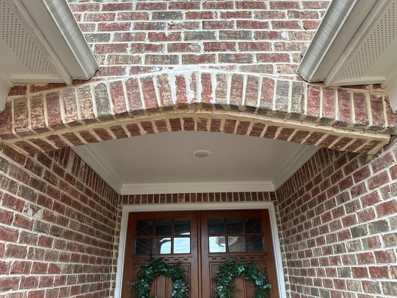 Cracked brick arch above a front entry door with an open mortar joint and efflorescence staining before Madewell repair