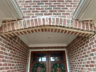 Cracked brick arch above a front entry door with an open mortar joint and white efflorescence staining at the crown