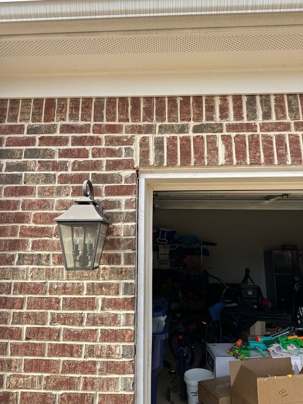 Vertical crack running through brick and mortar beside a garage door opening next to an exterior light fixture