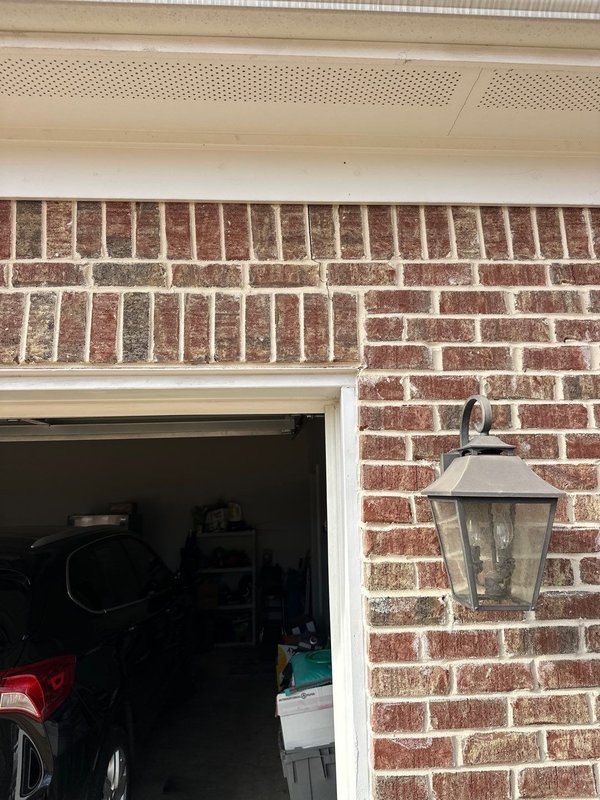 Close-up of a cracked brick course above a garage door opening near an exterior light fixture