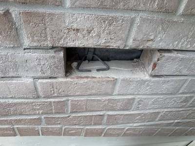 Close-up of a wall tie anchor and steel plate exposed in a cutout behind brick veneer on a Madewell masonry job