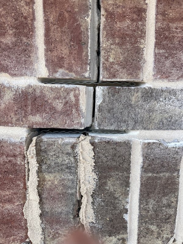 Close-up of corrugated metal wall ties anchoring brick veneer to the structure with fresh mortar packed around them