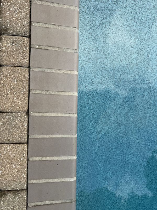 Brick pool coping with fresh mortar joints running between the paver deck on one side and the pool water on the other