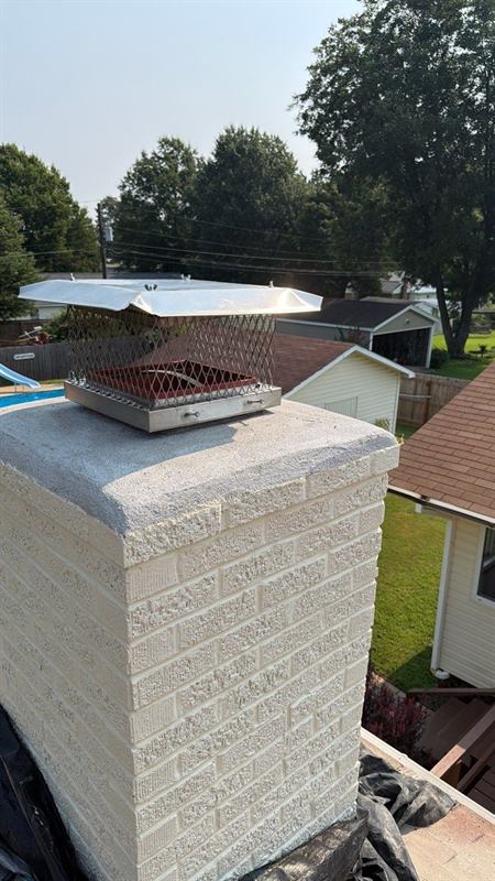 Stainless chimney cap on a painted brick chimney with the top-sealing damper plate visible inside the spark-arrestor mesh