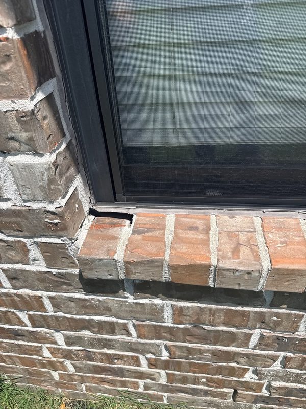 Missing brick at a window sill corner with an open joint at the jamb, leaving a gap under the window frame on a Memphis brick wall