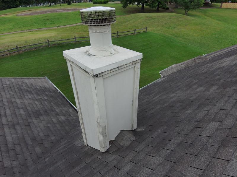 Weathered wood-framed chimney chase with damaged base flashing before repair