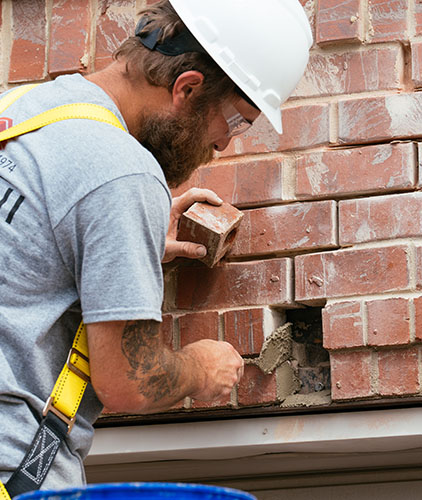 man with white hard hat and harness fixing broken masonry