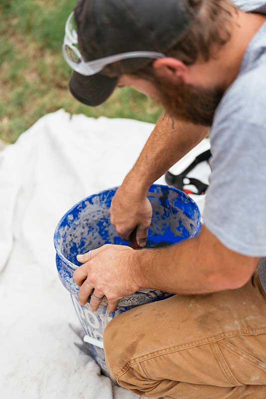 man with blue bucket filled with mortar mixing it