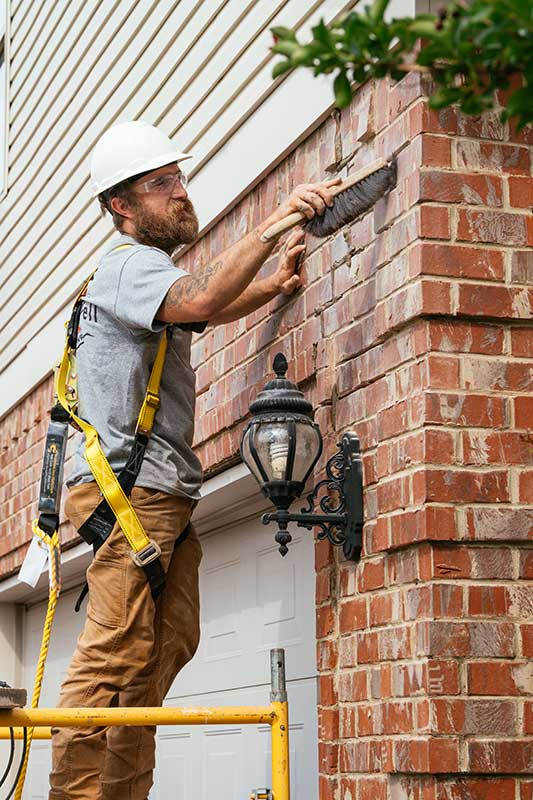 Man wearing harness and white helmet using tool to smooth masonry on side of home