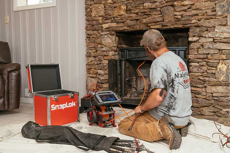 Man with hat and t shirt using equipment to inspect a chimney 