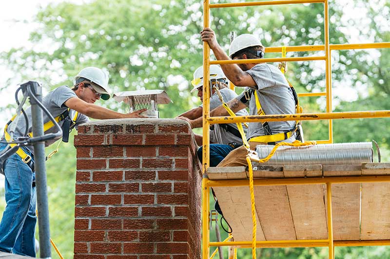 Three men working on chimney two on a yellow scaffold the other with a harness