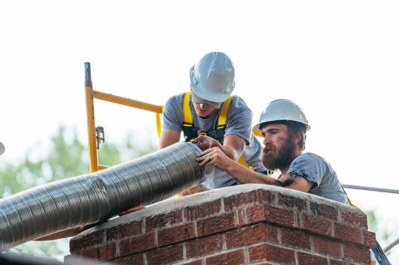 Two men wearing hardhats installing a new chinney liner on a chimney