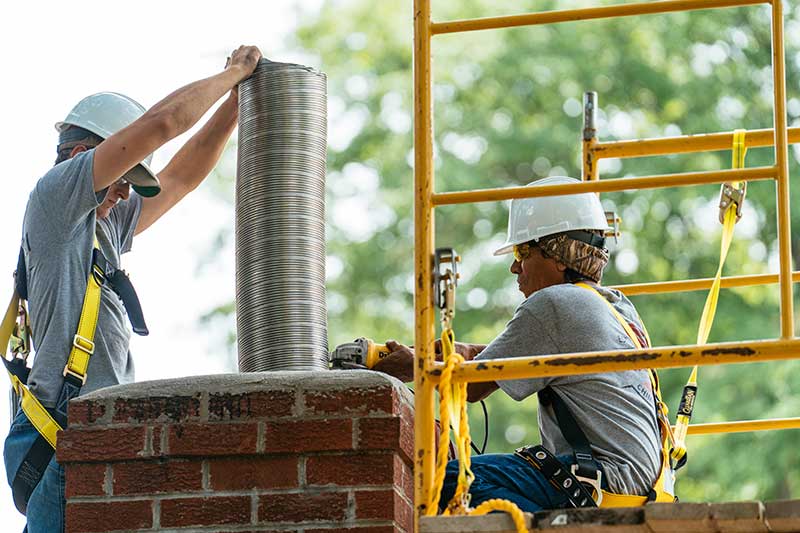 Two men wearing helmets and harnessess installing a new chimney liner