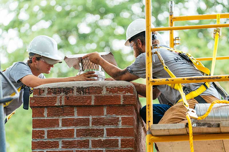 2 men installing a new chimney cap on a brick chimney