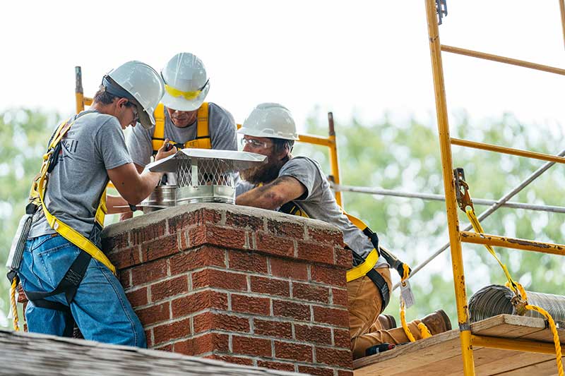 3 men installing a new chimney cap on a brick chimney