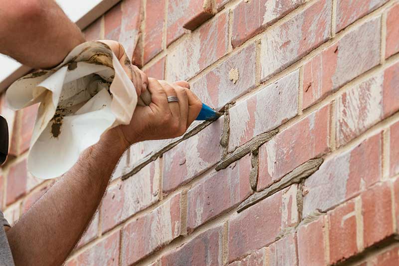 Two hands holding a tube or mortar and squeezing it onto a brick wall