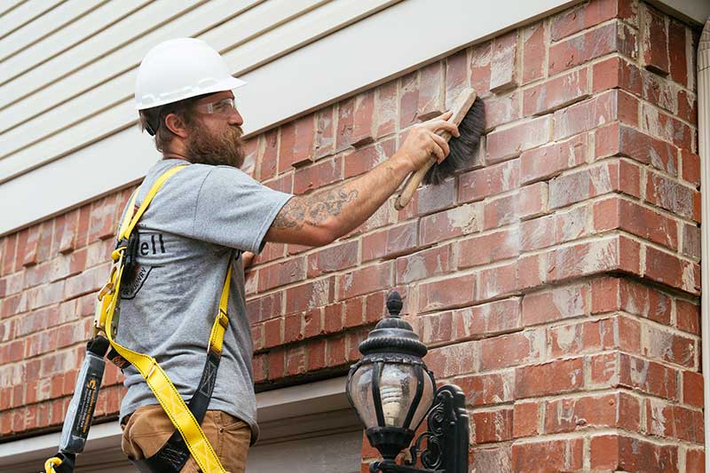 Man white white helmet and harness wiping off brick wall above garage