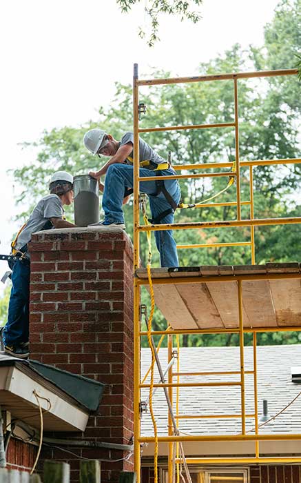 Two men standing on a platform and roof of a house putting a new liner in a chimney